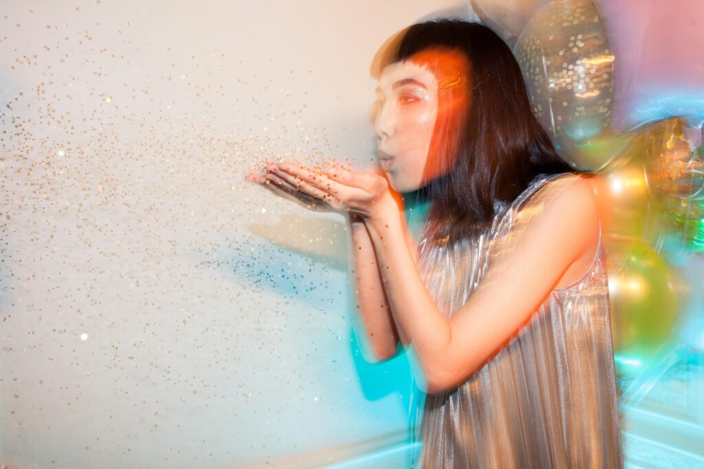 A fashionable woman blows glitter at a party, capturing a joyful and festive moment.